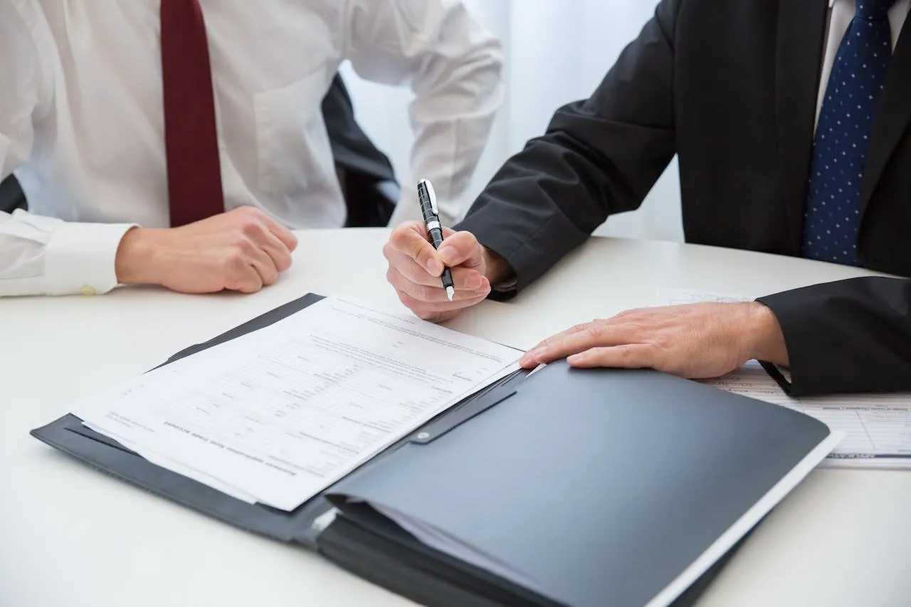 Two person sitting on a desk, man with suit filling up a form